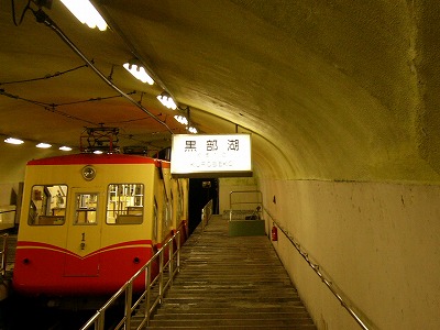赤と黄色の配色のケーブルカーと黒部湖駅の駅名標
