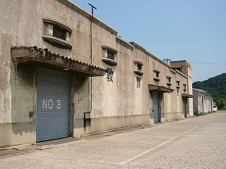 薄茶色く汚れた2階建てのコンクリートの倉庫。