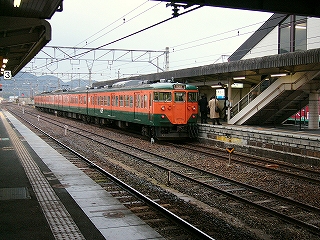 斜め向かいのホームに停車中の緑と橙の4両編成の列車。