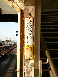 階段上り口脇の柱に取り付けられた縦長で小ぶりな古いホーローの大阪商事の広告看板。