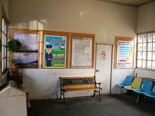 大きなポスター4枚、一人掛けの椅子4連、長椅子一つの駅舎内。