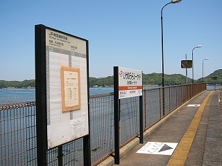 海辺の柵に沿って立てられた時刻表と駅名標。両方とも明かりはつかない。