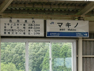 上屋から吊られた白地に黒い字で書かれた無灯式名所案内板とJR西日本様式の無灯式駅名標。上屋と壁に接近して吊られている。