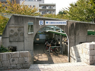 コンクリート打ち放しの小さなアーチの門の向こうに二段式で小規模な駐輪所のスペースがある。