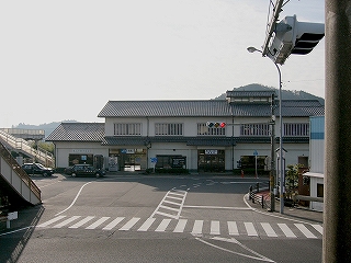 駅舎と駅前のアスファルトの敷地。左手端に構内を渡る跨線橋がちらっと移っている。