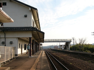 左手に白い壁の二階建ての頑丈なつくりの駅舎、遠くに跨線橋。