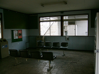 一人掛けの椅子が並ぶ寒々とした待合室内。灰色の壁、深緑の掲示板。