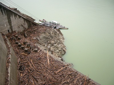 はるか下方のダム湖に幾艘かの船と岸上の大量の流木