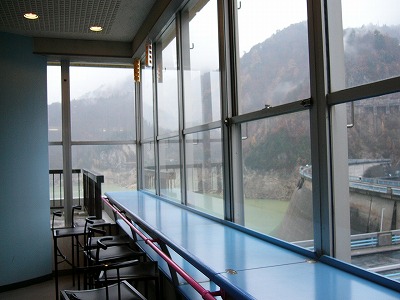 窓に沿って設置された水色の長いテーブルと椅子。窓からは黒部湖が。