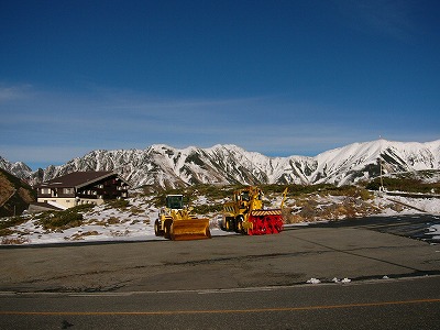 雪を少しかぶった奥大日岳連峰と立山高原ホテルと黄色の除雪車