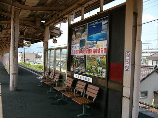 さまざまな景勝地を書いた「北陸本線・湖西線直通電車運行開始」の大きな宣伝広告の貼られた焦げ茶の背の高い風除け。その前に黄土色の3人座り椅子が2脚置いてある。