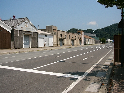 人も車も通らない太い道路の左脇に並ぶ古いコンクリートの倉庫。