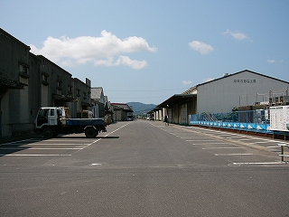 左右に2階建てぐらいの高さの倉庫。その間の敷地は舗装され、長々と駐車場が続いている。