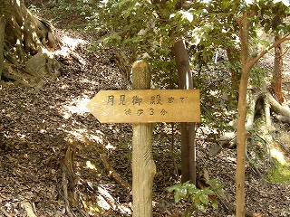 人工の薄茶の板に黒い字で「月見御殿まで徒歩3分」と彫られている。板は左側が三角になるように角を落とされてある。