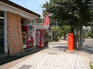 白タイルの歩道の左にすだれを立てかけた新しいお店、右に赤い古いポスト。