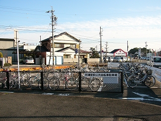 ロータリー中央部の端に作られた簡易な駐輪所。こげ茶の低いフェンスの向こうに自転車が並んでいる。