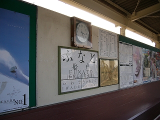 長椅子の背もたれの延長となった壁に駅名標と時計が掲げられている。