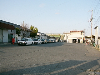 アスファルトの敷地。左の駅舎に沿ってタクシーが駐まっている。