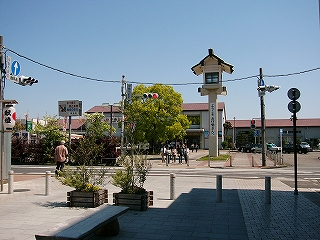 新緑の樹木と灯篭の背後に駅舎が垣間見える。