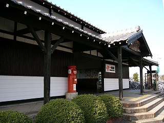 緑のつつじの植え込みと屋根瓦と黒い柱で組まれた駅の回廊。