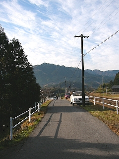 一台分ぐらいの幅の道。両脇に白い鉄パイプを二本並行させてできた柵。左手に緑の濃い木々、右手に停車場、正面ずっと遠くに高い山々。