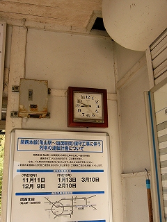駅舎の天井隅付近のようす。天井から少し下がった所に焦げ茶の太い枠の正方形のアナログの時計。その下に運休日を知らせる大きな白い紙に青い字で書かれたポスター
