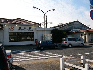低い三角錐の屋根の下にJR亀山駅と黒い字で表示された駅舎の右は知り部分と渡ってきた横断歩道。