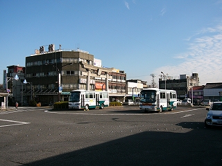 ロータリーの中央部にバス2台、その左に大きな石造りの鳥居。その左手にはコーナーに立つ坂本屋旅館の古いビル。ビルの屋上には「旅館」と書かれた大きな電飾文字が設置されてある。