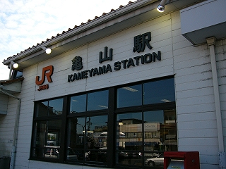 駅舎の壁は横長の白い板で作られ、そこにJR東海亀山駅と黒地で表示されている。駅名表示の下には待合室の窓ガラスの並び。