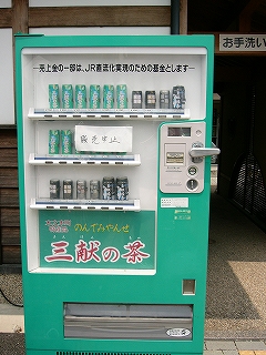 エメラルドグリーン色の自動販売機。わずかな種類の缶が幾つかずつ並べられている。
