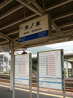 上屋から吊られたJR様式の電照式駅名標とその下にホームに立つ２つの駅名標。