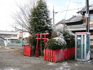 赤い柵のされた小さなスペース。常緑樹が茂り、入口には小さな鳥居が立てられている。
