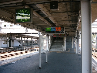 手前に時刻表。奥に跨線橋への階段。上り口上部には4色で色分けされた番線案内が吊られている。