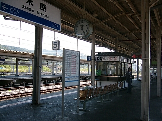 上屋下から、吊るされた駅名標、時刻表、椅子、駅そば屋を右斜めに見て。