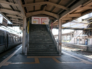 跨線橋階段上り口前。上り口の上からは矢印と小さな字が書かれた乗換案内板が吊られている。