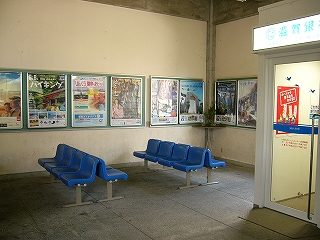 クリーム色に塗られた壁を巡らすようにポスターが貼られ、その前に青色の椅子が置かれている。