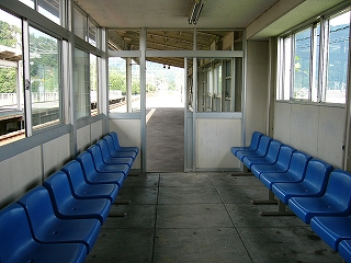 両脇に水色の一人掛け椅子が並んだ小さなプレハブ風の待合室。床はコンクリート打ち放し。