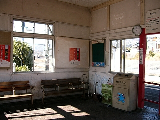 白い壁の駅舎内。3人がひとりひとり掛けられるいすが二つ。