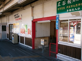 框が赤色に塗られた改札口。右上に三谷坂を宣伝する緑色の看板。