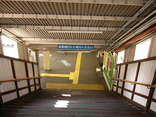 階段から駅舎内のアスファルトの地面を見下ろして。頭上の屋根も階段と並行に下がっている。