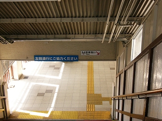 階段から駅舎の床を見下ろして。床は白色で、右から光が差し込んでいて明るい。