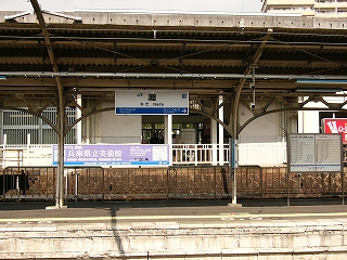 隣のホームの屋根から吊られた駅名標と、大きな四角に切り抜かれた駅舎の壁の内側を同時に見て。