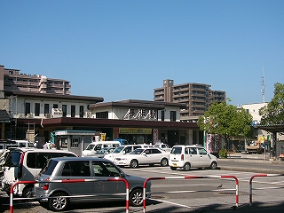 自動車が幾台も停まる駐車場とその向こうにある駅舎。