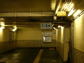 横長の長方形の地下道内。右上には細い配管が集められ、柔らかい光の蛍光灯がクリーム色の壁を照らしている。