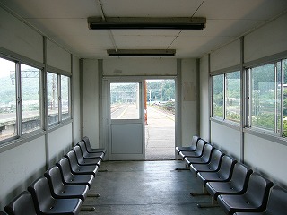 待合室の中。両端に窓、焦げ茶の並んだ椅子。