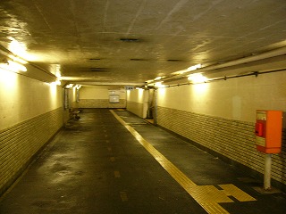 長方形の断面の地下道。蛍光灯証明がクリーム色の壁を陰気に照らす。