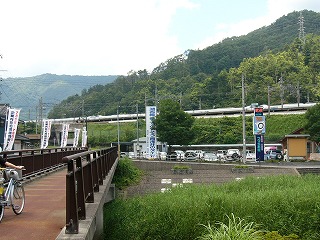 左に細い橋、川向こうに駅前駐車場と標語とつづらお荘の背の高い看板。