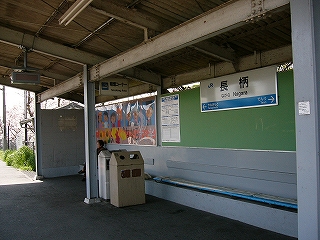 灰色の壁の待合所内。長椅子、子供らの描いた大きな絵、駅名標。