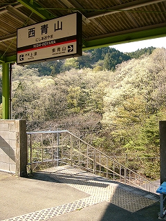 上屋から吊るされる駅名標と向こうの緑。