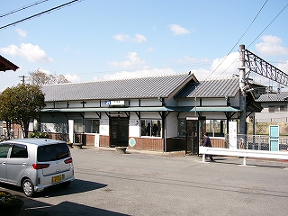 駅前のアスファルトの敷地と駅舎。駅舎の右手に架線柱。